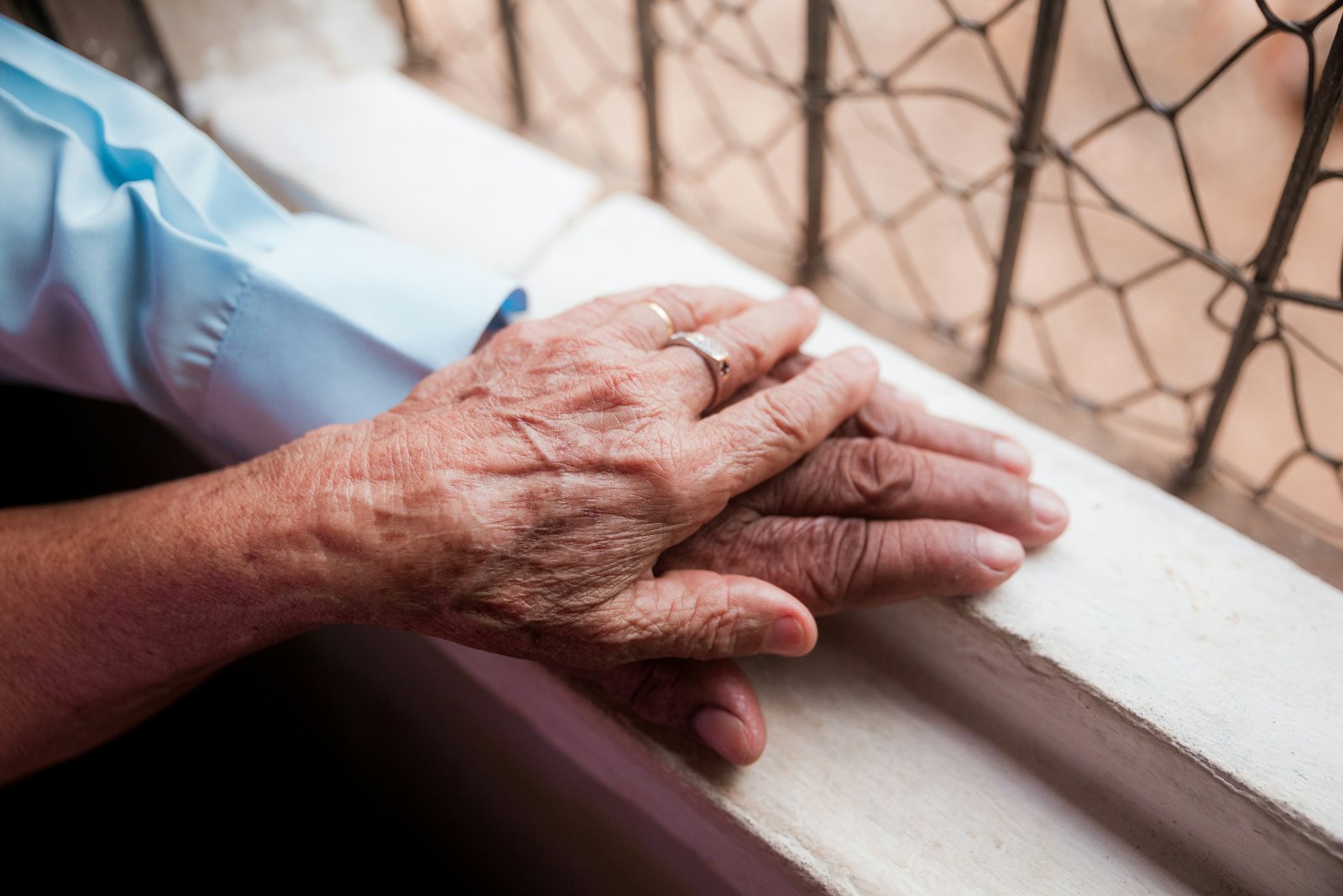 An older adult's hands resting on a windowsill